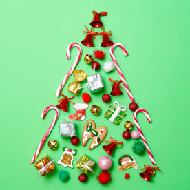 Large group of Christmas decoration items arranged in pattern in shape of Christmas tree on green background.