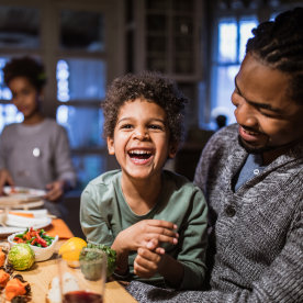 little boy laughing while at the dinner table in his father's arms 